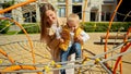 Young woman supporting her baby son climbing and playing on the playground with ropes and nets. Children playing outdoor, kids Royalty Free Stock Photo