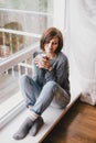 Young woman in a sweater and boyfriend jeans relaxing near big window Royalty Free Stock Photo