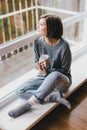 Young woman in a sweater and boyfriend jeans relaxing near big window Royalty Free Stock Photo