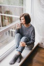Young woman in a sweater and boyfriend jeans relaxing near big window Royalty Free Stock Photo