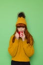 Young woman in sweater and cap with pompom is holding red mug