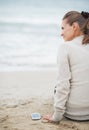 Young woman in sweater with cell phone sitting on lonely beach Royalty Free Stock Photo