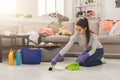 Young woman sweeping floor in messy room