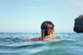 Young woman with swim goggles, surrounded by sea, view from behind, rocky cliff and clear sky background Royalty Free Stock Photo