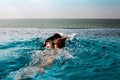 Young Woman swimming crawl style in a pool with sea view and blue sky