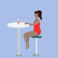 Young woman in a swimsuit drinking a cocktail at a table in a cafe