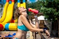 Young woman in a swimsuit drinks water from a bottle. Charming tanned athletic woman stands in the sun in a swimsuit and drinks