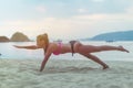 Young woman in swimsuit exercising on beach stretching her legs during sunset at sea. Fitness girl doing exercises on Royalty Free Stock Photo