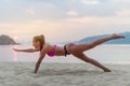 Young woman in swimsuit exercising on beach stretching her legs during sunset at sea. Fitness girl doing exercises on Royalty Free Stock Photo