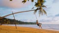 Young woman swinging sitting on swing at palm tree on sand beach at tropical sea in sunset lights. Happy girl enjoy Royalty Free Stock Photo
