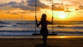 Young woman swinging sitting on wooden swing with ropes on sandy beach, sea sunset background. Girl silhouette enjoy Royalty Free Stock Photo