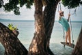 A young woman is swinging on a swing in the shade of a big tree by the sea. Royalty Free Stock Photo