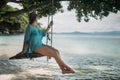 A young woman is swinging on a swing in the shade of a big tree by the sea. Royalty Free Stock Photo