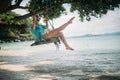 A young woman is swinging on a swing in the shade of a big tree by the sea. Royalty Free Stock Photo