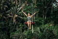 BALI, INDONESIA - MAY 16, 2018: Young woman swings in the jungle of Bali island. Rainforest of Indonesia. Travel concept