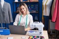 Young woman tailor smiling confident using laptop at clothing factory