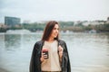 Young woman with take away coffee in hand in casual clothes near river water