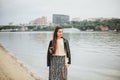 Young woman with take away coffee in hand in casual clothes near river water