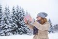 Young woman takes photo on a background of snow-covered winter forest. Royalty Free Stock Photo