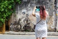 Young woman taking a photo of Street Art mural boy and girl on bicycle on a wall in George Town on Penang island in Malaysia