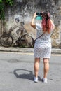 Young woman taking a photo of Street Art mural boy and girl on bicycle on a wall portrait format in George Town on Penang island Royalty Free Stock Photo