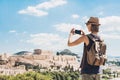 Young woman taking photographs with smart phone in Athens with Acropolis at the background. Traveler girl enjoy vacation in Greece