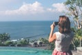 Young woman taking photos on the cliff with a beautiful ocean background at sunny day. Bali island. Royalty Free Stock Photo