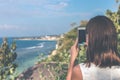 Young woman taking photos on the cliff with a beautiful ocean background at sunny day. Bali island. Royalty Free Stock Photo