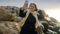 Young woman taking photos or herself at the winter sea using her smartphone while standing on the rocky shore. Perfect for travel Royalty Free Stock Photo