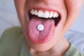 Young woman taking pill. Closeup of white round pill on tongue. Open mouth holding tablet