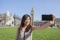 Young woman taking self portrait through smart phone against Big Ben at London, England, UK