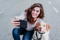 young woman taking a selfie with mobile phone with her dog at the street. autumn season Royalty Free Stock Photo