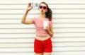 Young woman taking selfie picture by smartphone with coffee cup blowing red lips sending sweet air kiss wearing red heart shaped Royalty Free Stock Photo