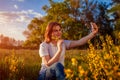 Young woman taking selfie in spring blooming field at sunset. Happy smiling girl relaxes and enjoys nature Royalty Free Stock Photo