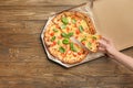 Young woman taking slice of delicious pizza Margherita from carton box on table Royalty Free Stock Photo