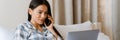 Young woman talking on cellphone and using laptop while lying in bed Royalty Free Stock Photo