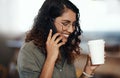 Young woman talking on her phone, drinking coffee, and smiling in cafe shop. Lady wearing glasses, using technology to Royalty Free Stock Photo