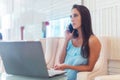 Young woman talking on mobile phone and smiling, sitting in front of the laptop in white hotel lobby Royalty Free Stock Photo