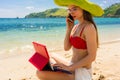 Young woman talking on mobile phone while using a tablet on the beach Royalty Free Stock Photo