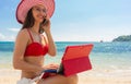 Young woman talking on mobile phone while using a tablet on the beach Royalty Free Stock Photo