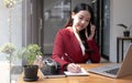 Young woman talking on mobile phone and writing notes while sitting at her desk. Asianfemale working in home office Royalty Free Stock Photo