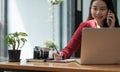 Young woman talking on mobile phone and writing notes while sitting at her desk. Asianfemale working in home office Royalty Free Stock Photo