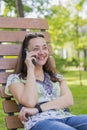 Young woman talking on the smartphone and laughing in the park on the bench Beautiful female relaxing on a park bench and using a Royalty Free Stock Photo