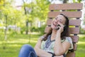 Young woman talking on the smartphone and laughing in the park on the bench Beautiful female relaxing on a park bench and using a Royalty Free Stock Photo