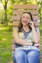 Young woman talking on the smartphone and laughing in the park on the bench Beautiful female relaxing on a park bench Royalty Free Stock Photo