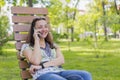 Young woman talking on the smartphone and laughing in the park on the bench Beautiful female relaxing on a park bench and using a Royalty Free Stock Photo