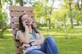 Young woman talking on the smartphone and laughing in the park on the bench Beautiful female relaxing on a park bench and using a Royalty Free Stock Photo