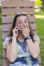 Young woman talking on the smartphone and laughing in the park on the bench Beautiful female relaxing on a park bench and using a Royalty Free Stock Photo