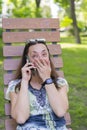 Young woman talking on the smartphone and laughing in the park on the bench Beautiful female relaxing on a park bench and using a Royalty Free Stock Photo