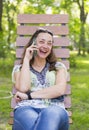 Young woman talking on the smartphone and laughing in the park on the bench Beautiful female relaxing on a park bench and using a Royalty Free Stock Photo